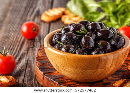Fresh olives with toasted baguette on a wooden board.