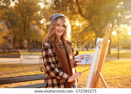 Young female artist painting picture in autumn park