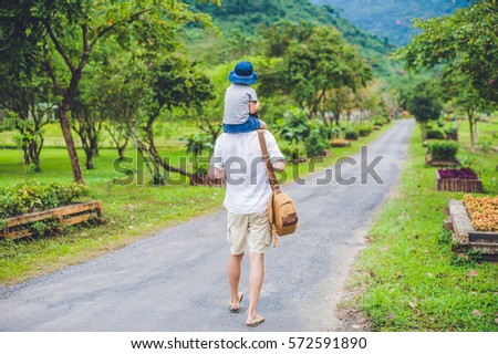 rear view of father and son walking on a scenic road.