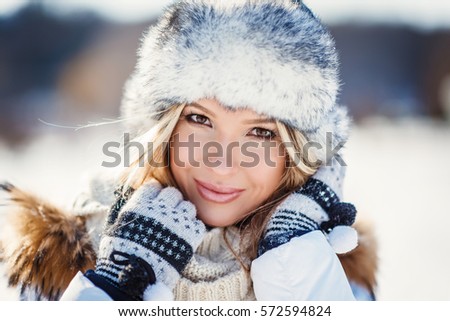 Winter portrait of young beautiful blond woman wearing knitted snood covered in snow. Snowing winter beauty fashion concept.