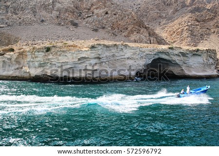 Men on a speedboat passing by a rocks with little cave in Oman
