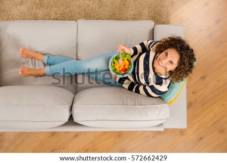 Top view of a beautiful woman on the sofa eating a healthy salade Royalty-Free Stock Photo #572662429