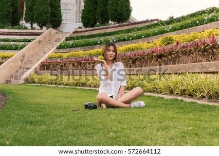 Young beautiful hipster woman sitting on the grass in the park and holding green apple in hand.