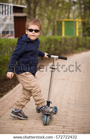 Cute small boy in sun glasses and scooter in a park. Riding a scooter. Kids activities outdoor.