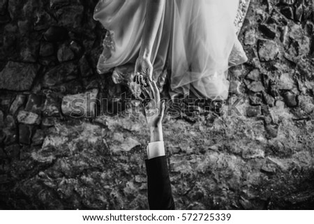 Black and white picture of hands of bride and groom touching each other over the pavement