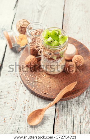 Fresh kiwi fruit, cashew, flax seeds and walnuts overnight oatmeal in jar and ingredients on a white wooden table. Close up and selective focus. Toned picture