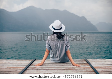 Beautiful woman relaxing on pier in Garda Lake. Vacation concept Royalty-Free Stock Photo #572736379