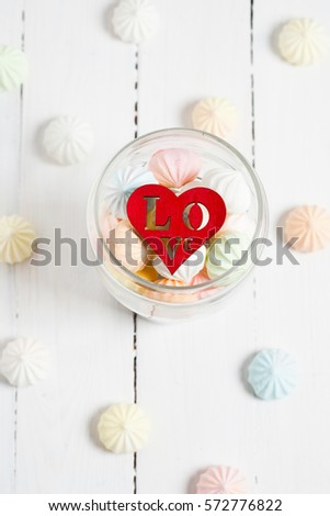 Color zephyrs and wooden figure of heart in glass jar on white wooden table. Concept of St. Valentine's Day