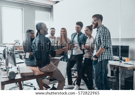 Young professional team.  Group of young modern people in smart casual wear having a brainstorm meeting while standing behind the glass wall in the creative office Royalty-Free Stock Photo #572822965