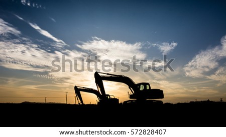 Silhouette of excavator at construction site in oilfield - sunset Royalty-Free Stock Photo #572828407