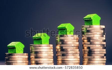 Small green houses standing on stacks of coins. Royalty-Free Stock Photo #572835850