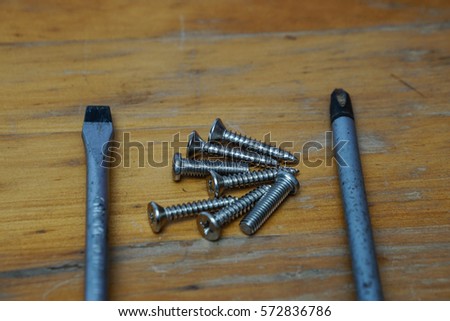 a pair of screw diver and bunch of screws on wood background