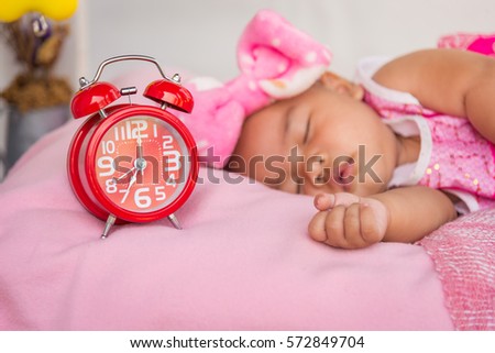 Red alarm clock on small bed with baby sleeping.