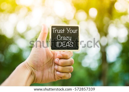 Trust Your Crazy IDEAS word on Black Board with hand hold the board. Hands show Good Sign.