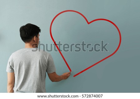 Man drawing  heart for valentines day with red chalk on wall. Close up.