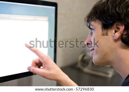 A young man pointing at a modern computer monitor lcd with copy-space.  Shallow depth of field with strongest focus on the face.
