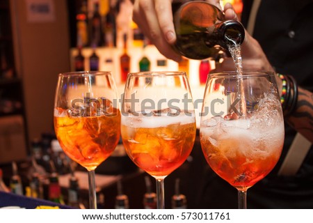 three glasses of cocktails on the bar. bartender pours a glass of sparkling wine with Aperol. Royalty-Free Stock Photo #573011761