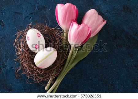 Easter eggs in the nest and pink tulips on rustic dark blue background,spring holiday concept