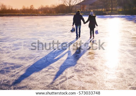 Couple in love walking on the ice with skates in hands during calm winter sunset - active wallpaper for valentine