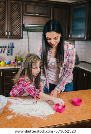 happy mother baking with little daughter in apron and cook hat working with flour , bowl and spoon preparing dough teaching the kid cooking and having fun together