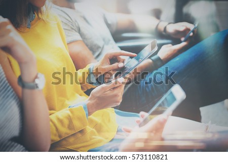 Group of young hipsters sitting on sofa holding en hands and using digital tablet,smartphone.Coworking team concept.Horizontal,blurred background Royalty-Free Stock Photo #573110821