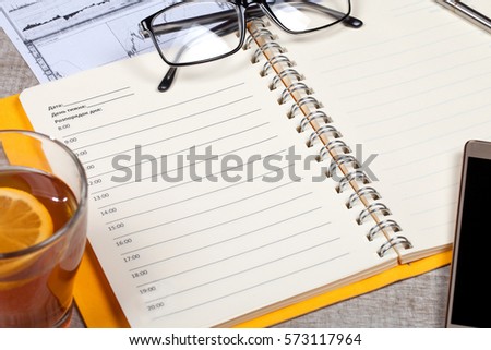 Top view of open notebook, glasses, a cup of tea, pen and smartphone on a wooden table. Close-up