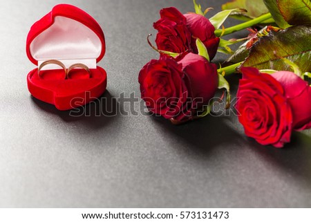 Beautiful red roses bouquet and wedding rings on a black background. Postcard for Valentine day or Wedding. Free space for text.
