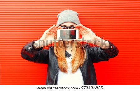 Fashion cool girl taking picture on smartphone self portrait, screen view, over red background
