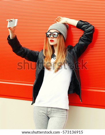 Fashion girl taking self-portrait on smartphone in city over red background