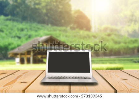 Laptop with blank screen on wooden table with Cottage in the rice field background, can used for display or montage your products