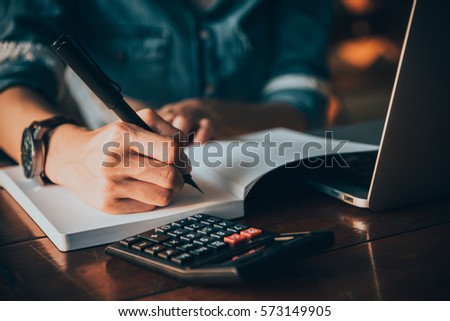Close up of people hand writing on the notebook on the table with laptop and mobile phone 