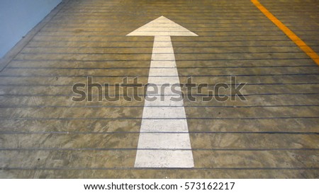 White arrow sign on a sloped concrete floor.