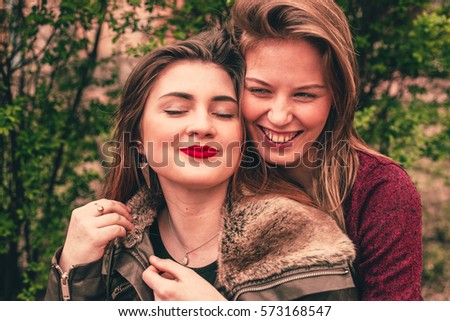 Two Young Friends girls blonde and brunette  sitting in the park and talking about something, girlfriends gossip, happy chilling lifestyle and people concept: happy teenagers making funny faces