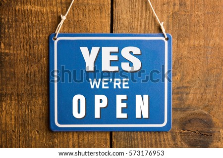 " YES we're OPEN " sign in blue and white, on rustic wooden wall.