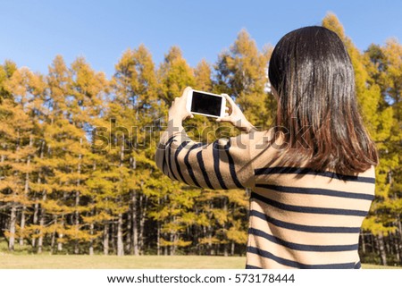 Woman taking photo by cellphone in autumn forest