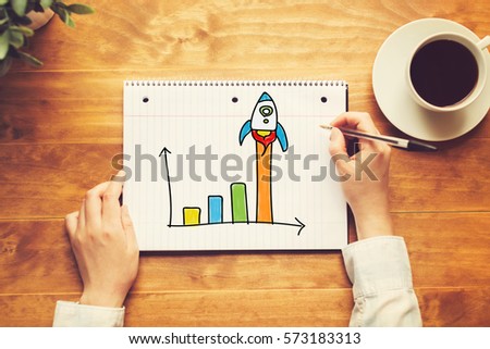 Rocket Graph with a person holding a pen on a wooden desk