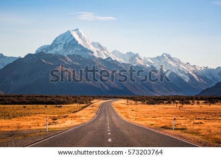 A long road leading to a large snow capped mountain on a sunny day Royalty-Free Stock Photo #573203764