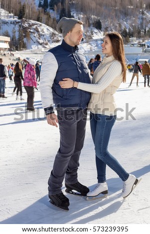 Loving couple skating together holding hands. Mountains in the background