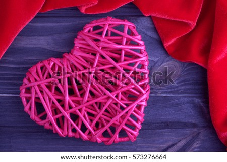 Pink wicker heart on a brown wooden background with red fabric frame, vintage