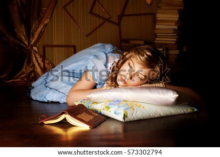 Little girl in a blue dress sleeping on the floor in room, beside her is a book