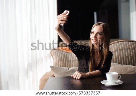 Young pretty woman with beautiful smile posing while photographing herself on mobile phone camera