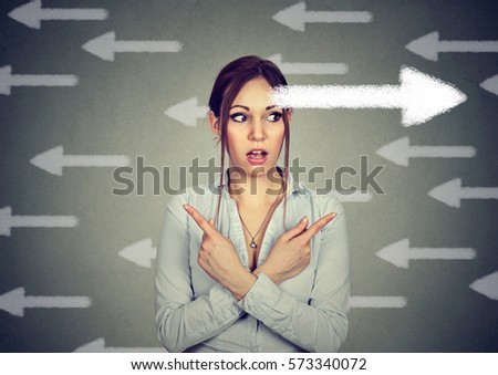 Young woman has a second thought choice perplexed pointing fingers in two different direction  Royalty-Free Stock Photo #573340072