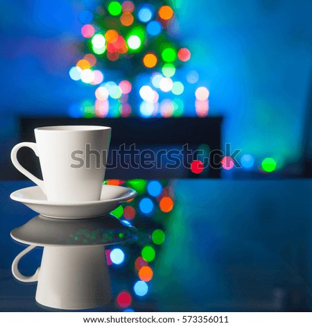 White coffee cup and saucer on a glass table on the background colorful bokeh. Image about family holiday evenings and coziness. For printed materials and backgrounds.