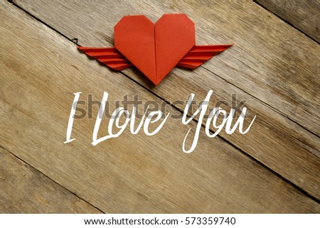 Valentine concept. Red paper origami heart with wings with I LOVE YOU written on wooden background.