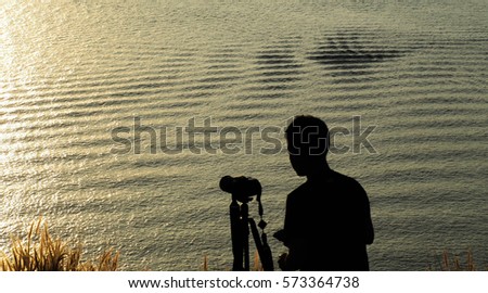 The sun shine over the sea with golden brown color above the ocean with a silhouette of a man with camera for sunset picture.