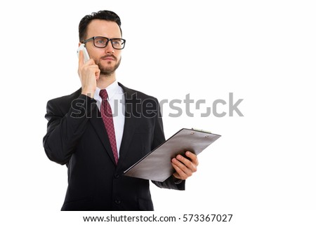 Studio shot of young businessman holding clipboard and talking on mobile phone