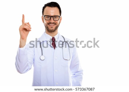 Studio shot of young happy man doctor smiling while pointing finger up