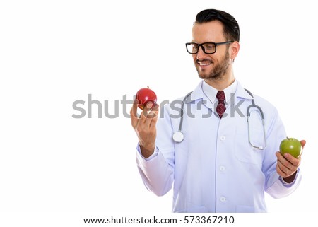 Studio shot of happy young man doctor smiling while looking at red apple and holding green apple