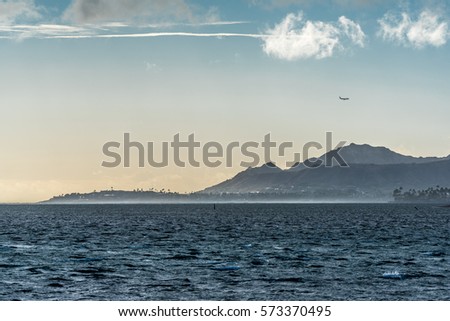 late afternoon view on a windy day of Diamond Head crater and black point peninsula, taken from Maunalua Bay in Hawaii Kai, Oahu, Hawaii with a commercial jet flying overhead