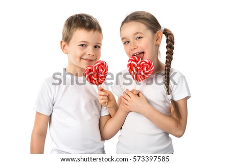 Cute kids little boy and girl in white T-shirts with candy red lollipops in heart shape, isolated on white background. Beautiful children eat sweets. Valentine's day, love concept.